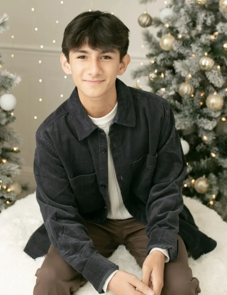 A young man sitting in front of christmas trees.